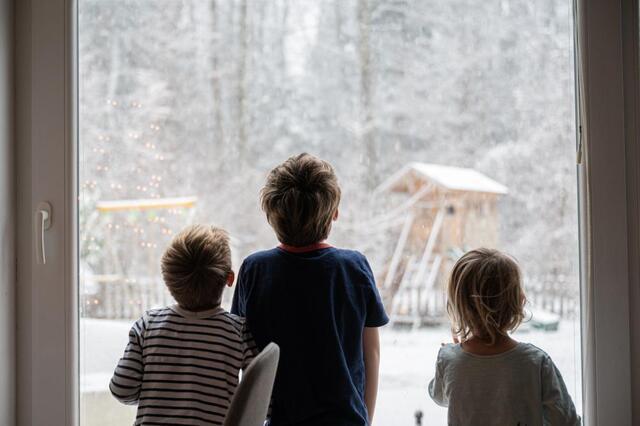 three children looking outside at the snow