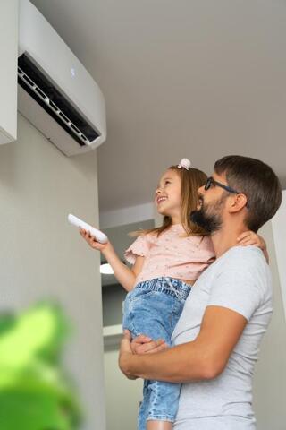 man lifting daughter up to use remote on heat pump